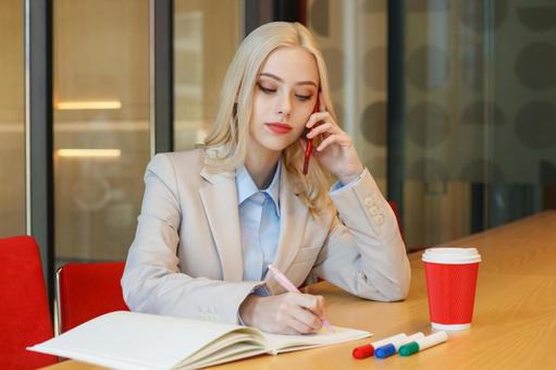 オフィスでノートにメモを取りながら電話する女性 ビジネスウーマン,ビジネス,女性の写真素材