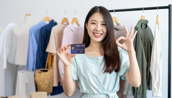 洋服を背景にカードを持ちOKサインの女性 洋服を背景にカードを持ちOKサインの女性の写真