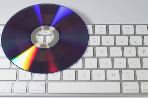 キーボード中央に置かれた虹色に輝くCD cd,コンパクトディスク,キーボードの写真素材