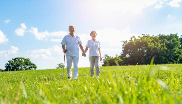 青空の下　草原を散歩するシニアの写真