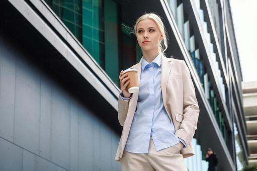 オフィスビルの外に居るコーヒーを持った外国人女性 ビジネスウーマン,ビジネス,女性の写真素材