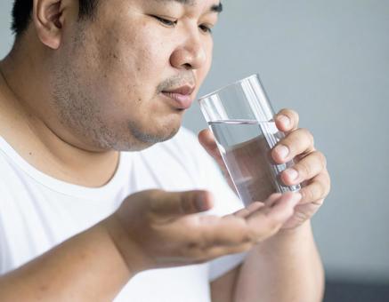 薬を飲む肥満男性 薬を飲む肥満男性の写真