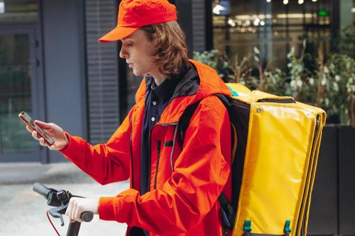 街なかでスマートフォンを使っているフードデリバリーの男性 配達,フードデリバリー,デリバリーの写真素材