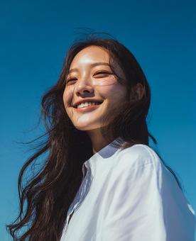 青空を見上げる若い女性の笑顔の写真