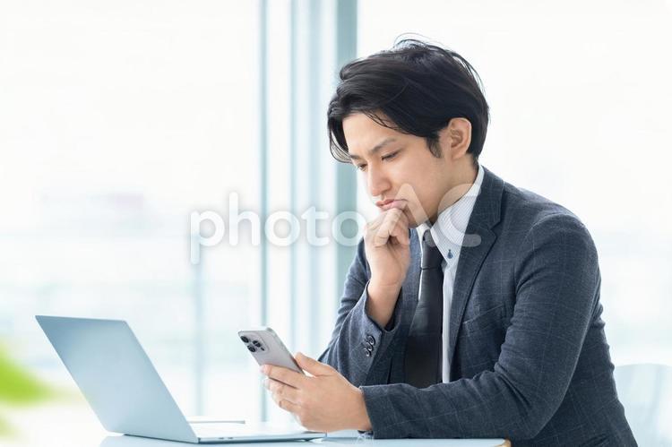 スマホを見て考える男性ビジネスマン 男性,考える,スマホの写真素材