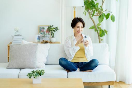 部屋でスマホを使うミドル女性 スマホ,笑顔,女性の写真素材