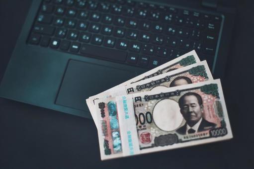 日本円の札束と開いたノートパソコン 日本円の札束と開いたノートパソコンの写真