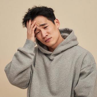 頭痛で困った表情を見せるパーカー姿の男性 頭痛で困った表情を見せるパーカー姿の男性の写真
