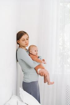 壁際で赤ちゃんを抱き目を瞑る女性 壁際で赤ちゃんを抱き目を瞑る女性 女性,赤ちゃん,かわいいの写真素材