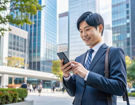 オフィス街でスマホを操作するビジネスマン オフィス街でスマホを操作するビジネスマンの写真