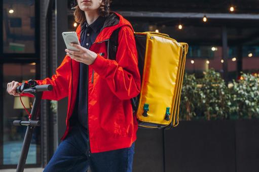 街なかでスマートフォンを見ている配達員の男性 配達,フードデリバリー,デリバリーの写真素材