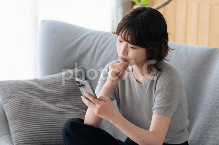 スマホを見ながら考えごとをする女性 女性,スマホ,スマートフォンの写真素材
