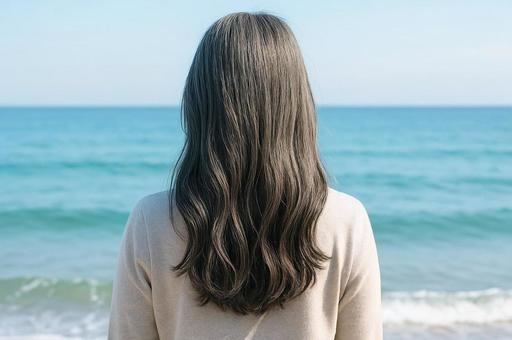ロングヘアの女性が海を見つめる後ろ姿の写真