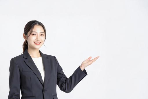 スーツ姿の若い女性が手で案内するイメージの写真