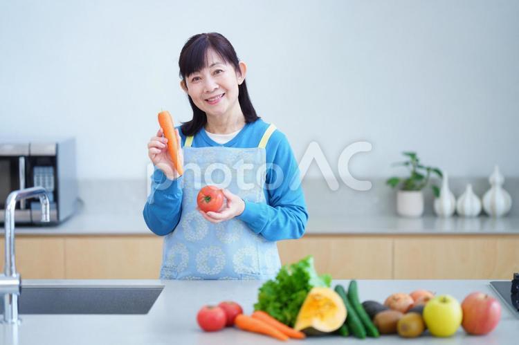 野菜を手にした笑顔の中年女性とキッチンシーン 主婦,家政婦,エプロンの写真素材