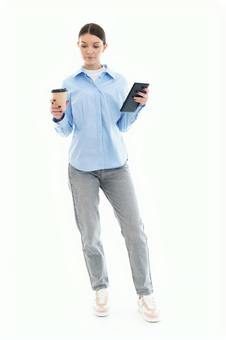 コーヒーとスマホを持ち立つ女性 コーヒーとスマホを持ち立つ女性の写真