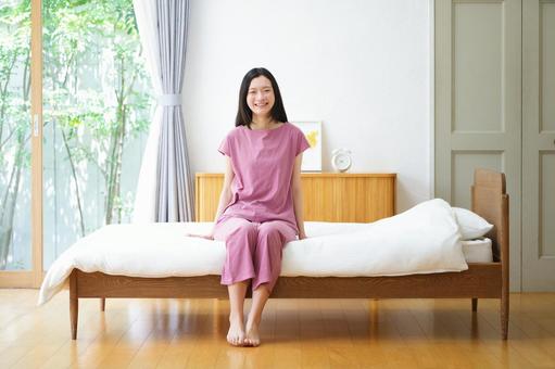 ベッドサイドに座り笑顔のカメラ目線女性 女性,ベッド,座るの写真素材