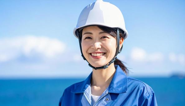 青空と海の背景に笑顔の作業服の若い女性の写真