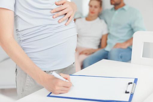 問診に記入する妊婦と後ろに夫婦 問診に記入する妊婦と後ろに夫婦の写真