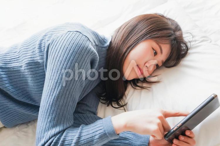 ベッドで寝る前にスマホを使う若い女性 投稿,休日,睡魔の写真素材