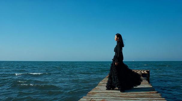 海を背景に黒いドレスを着た女性 海を背景に黒いドレスを着た女性の写真