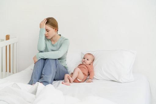 赤ちゃんを枕に寄り掛からせて悩む女性 育児疲れ,疲れた,座るの写真素材
