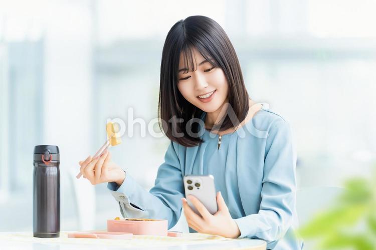 スマホを見ながらお弁当を食べる女性 女性,人物,ビジネスの写真素材