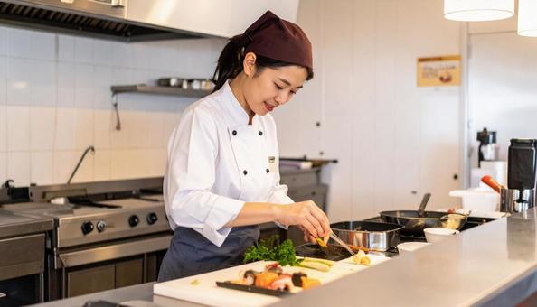 レストランの調理場で料理するスタッフ女性 レストランの調理場で料理するスタッフ女性の写真