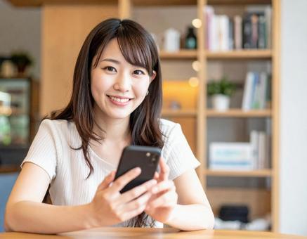 カフェでスマートフォンを操作する女性 カフェでスマートフォンを操作する女性の写真