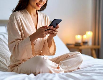 ベッドの上でスマホ見ている女性 ベッドの上でスマホ見ている女性の写真