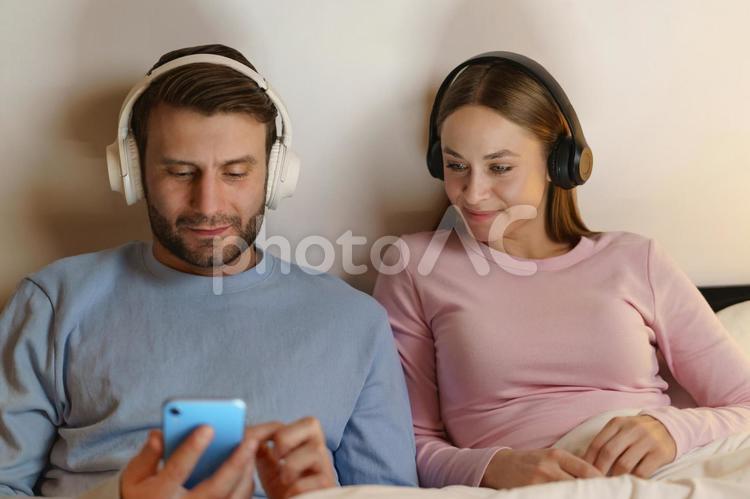 ヘッドフォンをして男性の携帯を見る女性 男性,女性,もたれるの写真素材