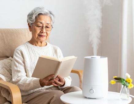 加湿器のそばで読書を楽しむシニア女性の写真