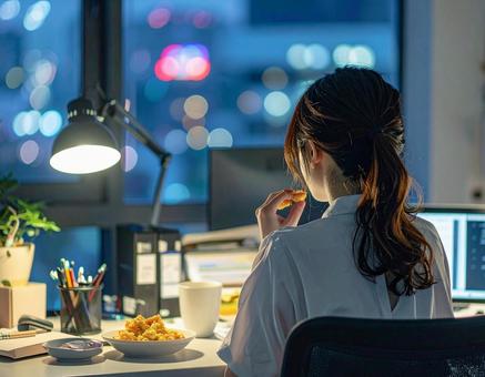 残業中にお菓子を食べる女性会社員の写真