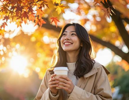 紅葉の中でコーヒーを持ち笑顔を見せる女性の写真