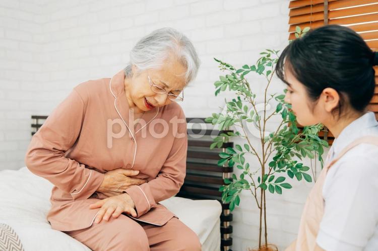 痛がる高齢者女性とエプロン姿の女性（腹痛） 高齢者,腹痛,お腹の写真素材