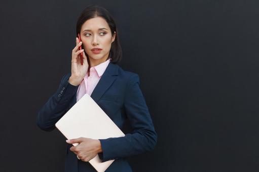 オフィスビルの黒い壁の前で電話している女性 ビジネスウーマン,ビジネス,女性の写真素材