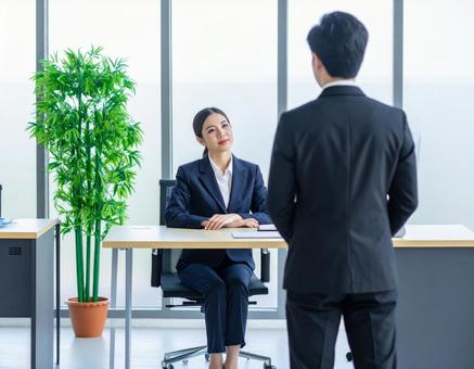 女性上司とその前に立つサラリーマンの部下 女性上司とその前に立つサラリーマンの部下の写真