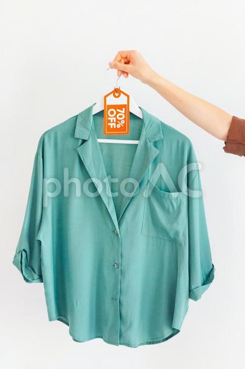 セールのタグの付いたハンガーに掛かった洋服を持っている女性の手 セール,ショップ,女性の写真素材