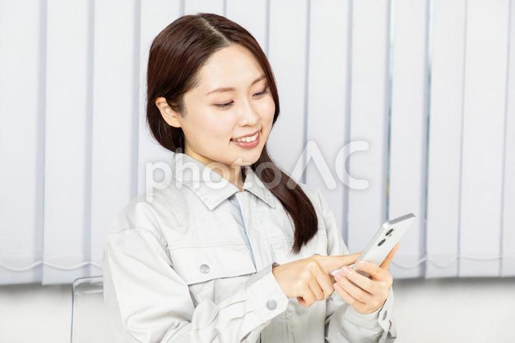 スマホを操作する作業服姿の女性03 作業員,女性,作業着の写真素材