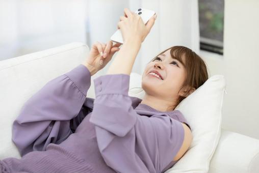 ソファーでスマホを使う女性 ソファーでスマホを使う女性 女性,人物,スマートフォンの写真素材