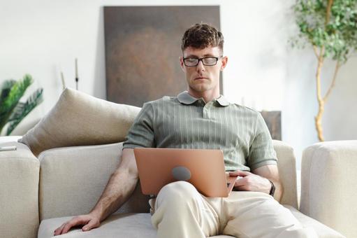 ソファに座って膝の上でノートパソコンを使う男性 男性,外国人,欧米人の写真素材