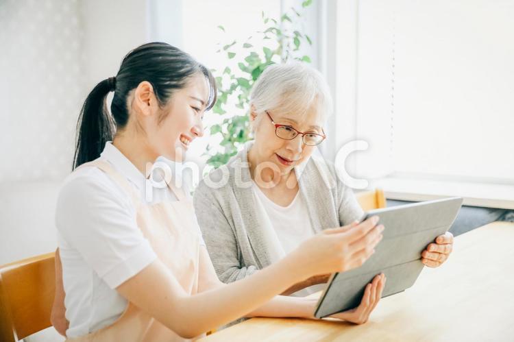 タブレットを使うエプロン姿の女性と高齢者女性 高齢者,介護士,タブレットの写真素材