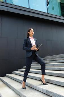 コーヒーとタブレットを持ってオフィスビルの外の階段を登るアジア人ビジネスウーマン ビジネスウーマン,ビジネス,女性の写真素材