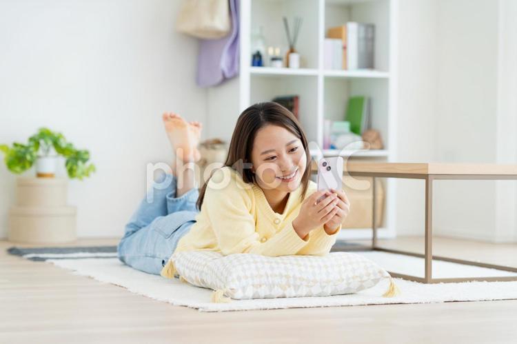 リビングでスマホを見る若い女性 リビングでスマホを見る若い女性 スマートフォン,女性,リビングの写真素材
