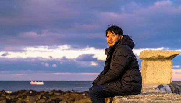 冬の空の下、一人旅を楽しみ石垣に座る男性の写真