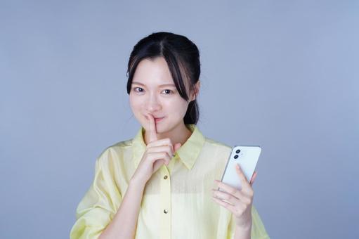 スマホをもって内緒のポーズをする黄色い服を着た女性 女性,スマートフォン,持つの写真素材