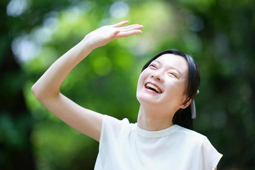 女性が日差しを避けるように手をかざす 女性,笑顔,眩しいの写真素材