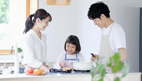 キッチンで料理を楽しむ母娘と見守る父親 キッチンで料理を楽しむ母娘と見守る父親の写真
