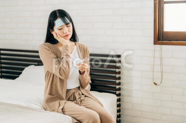ベッドで休む体調不良の女性（冷却シート・体温計・困る） 風邪,体温計,高熱の写真素材