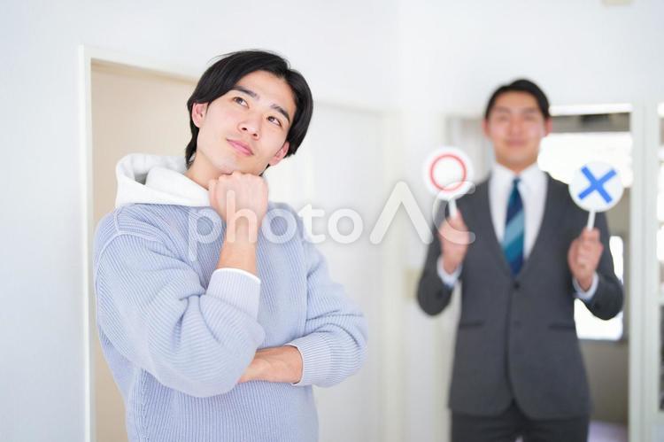 考えている内見中の男性とマルバツの札を持つ不動産営業マン 引っ越し,部屋探し,一人暮らしの写真素材